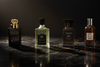 Gucci Intense Oud, Tom Ford Oud Wood, Creed Royal Oud and Hugo Boss Confident Oud The Collection bottles arranged on a dark marble surface in a luxury library setting